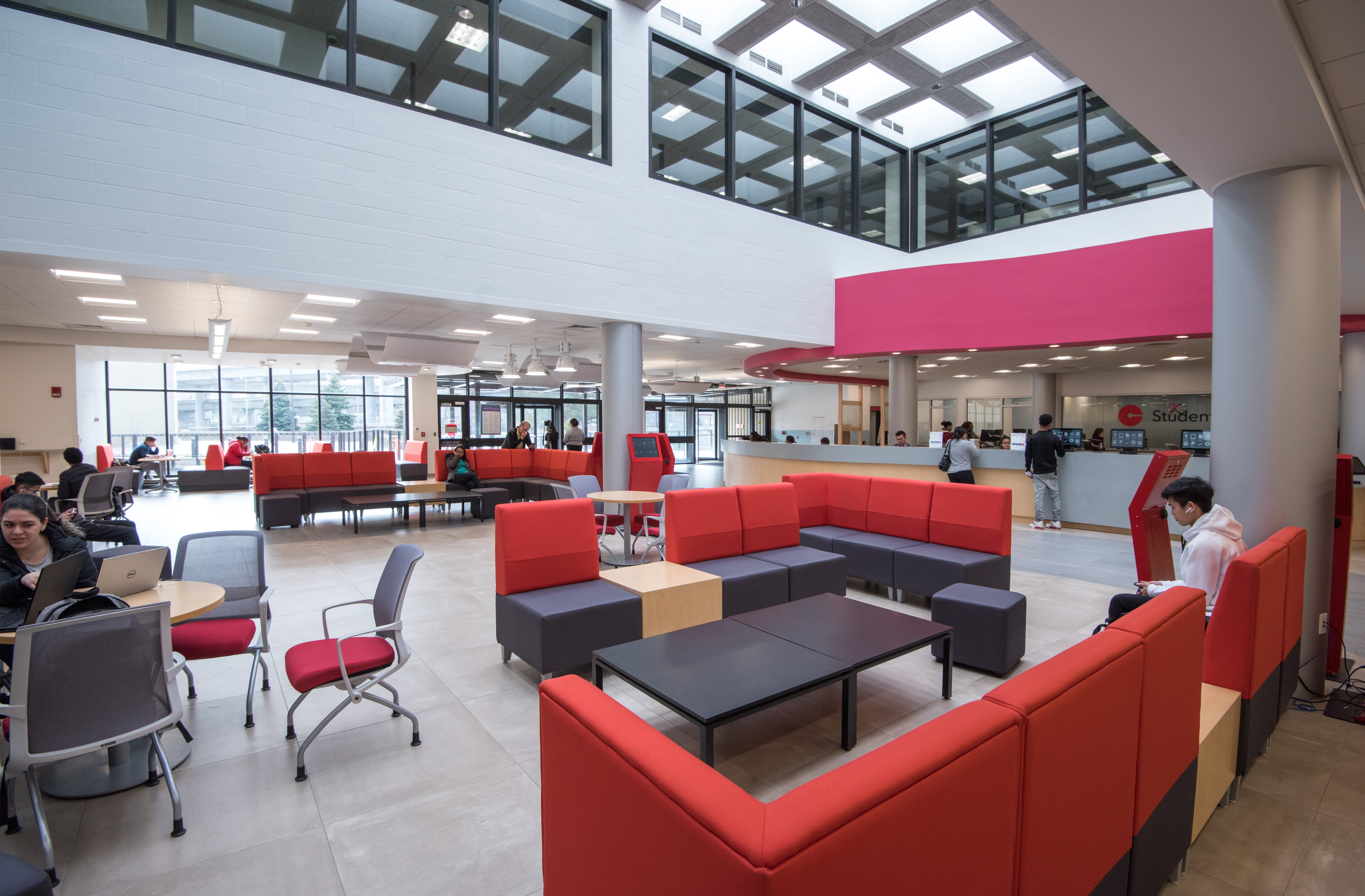 Student Central One Stop lounge area and student services area, at Bunker Hill Community College, longue seating and tables, chairs, café tables, student services desk, kiosks, students and staff occupy the space