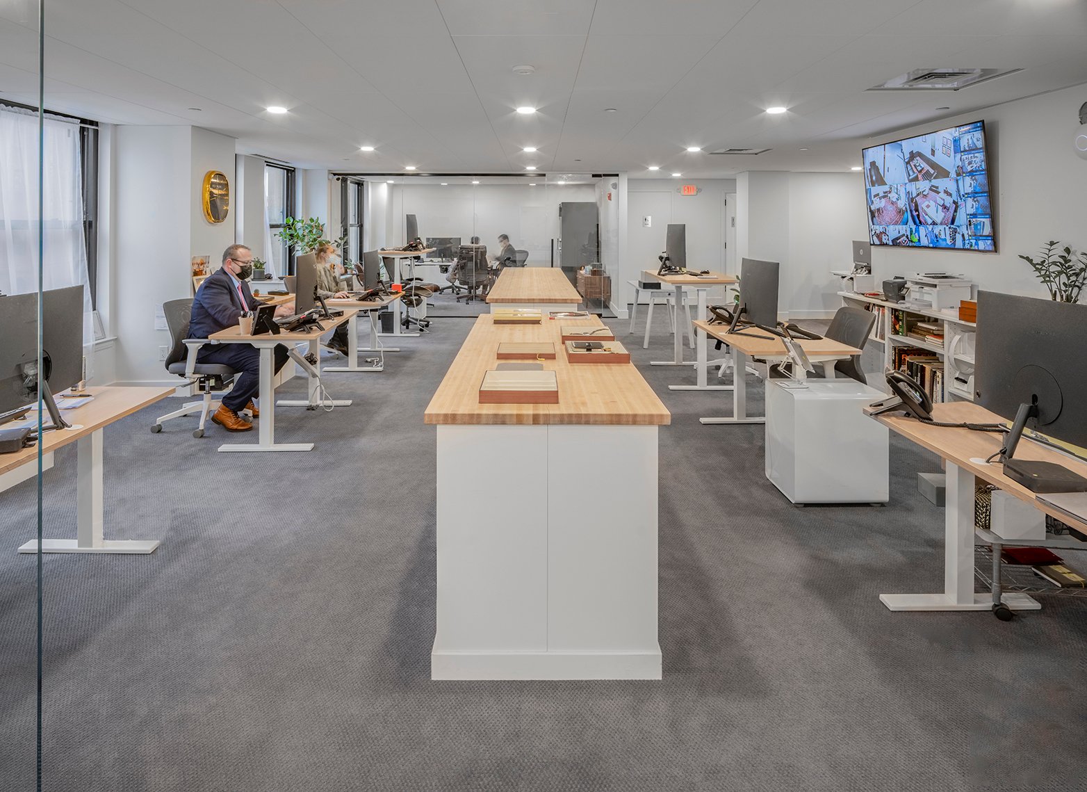 European Watch Company Client Area, desks with computers, some with employee occupying the desks, television mounted on the wall